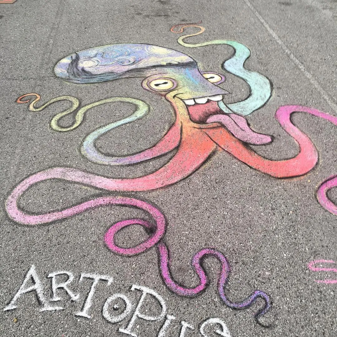 Chalk drawing on parking lot pavement. Drawing depicts a cartoony octopus-like creature with only four tentacles that fade through a rainbow of colors a wide-open smile with three large, rounded teeth, and a pink tongue hanging out. In the head-sac is a rendering of Picasso's A Starry Night painting.