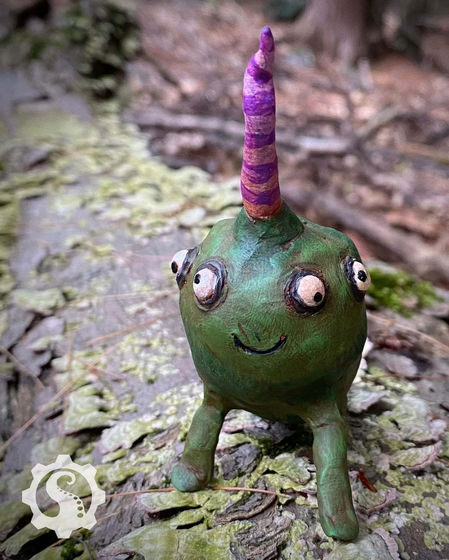Smiling green creature with four bulgy eyes looking in all different directions. A long pink and purple striped horn juts forward from the top of its head. He looks very friendly.