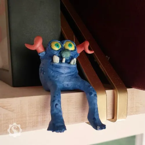 Sculpture of an original character monster that sits on a shelf with his legs hanging over the edge.